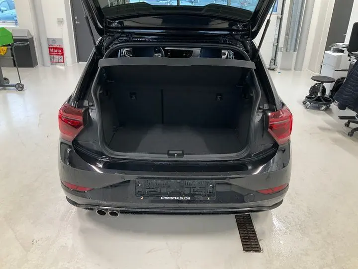 Vue arrière d'une Volkswagen Polo GTI noire 2024 avec coffre ouvert, double sortie d'échappement et feux arrière allumés.