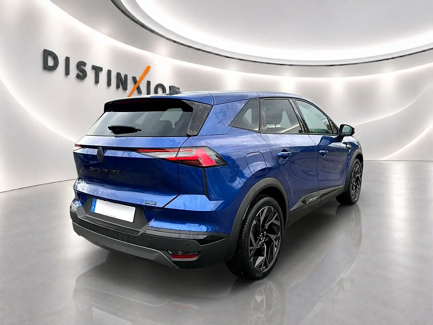Vue 3/4 arrière droite du Renault Symbioz bleu iron avec jantes noires et feux arrière LED fins dans un showroom moderne.