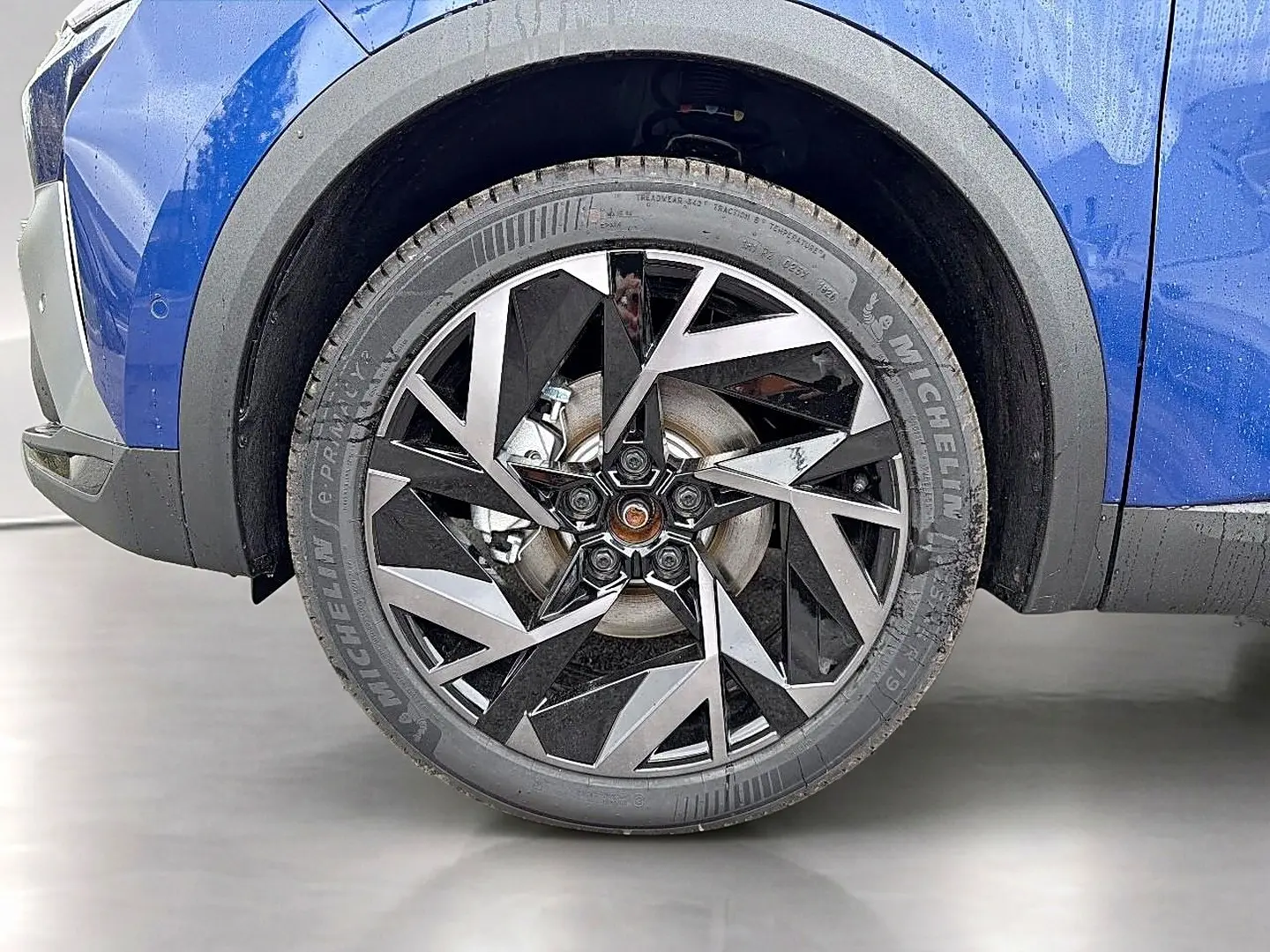 Gros plan sur la roue avant droite du Renault Symbioz bleu iron avec jante alu au design géométrique noir et argent.