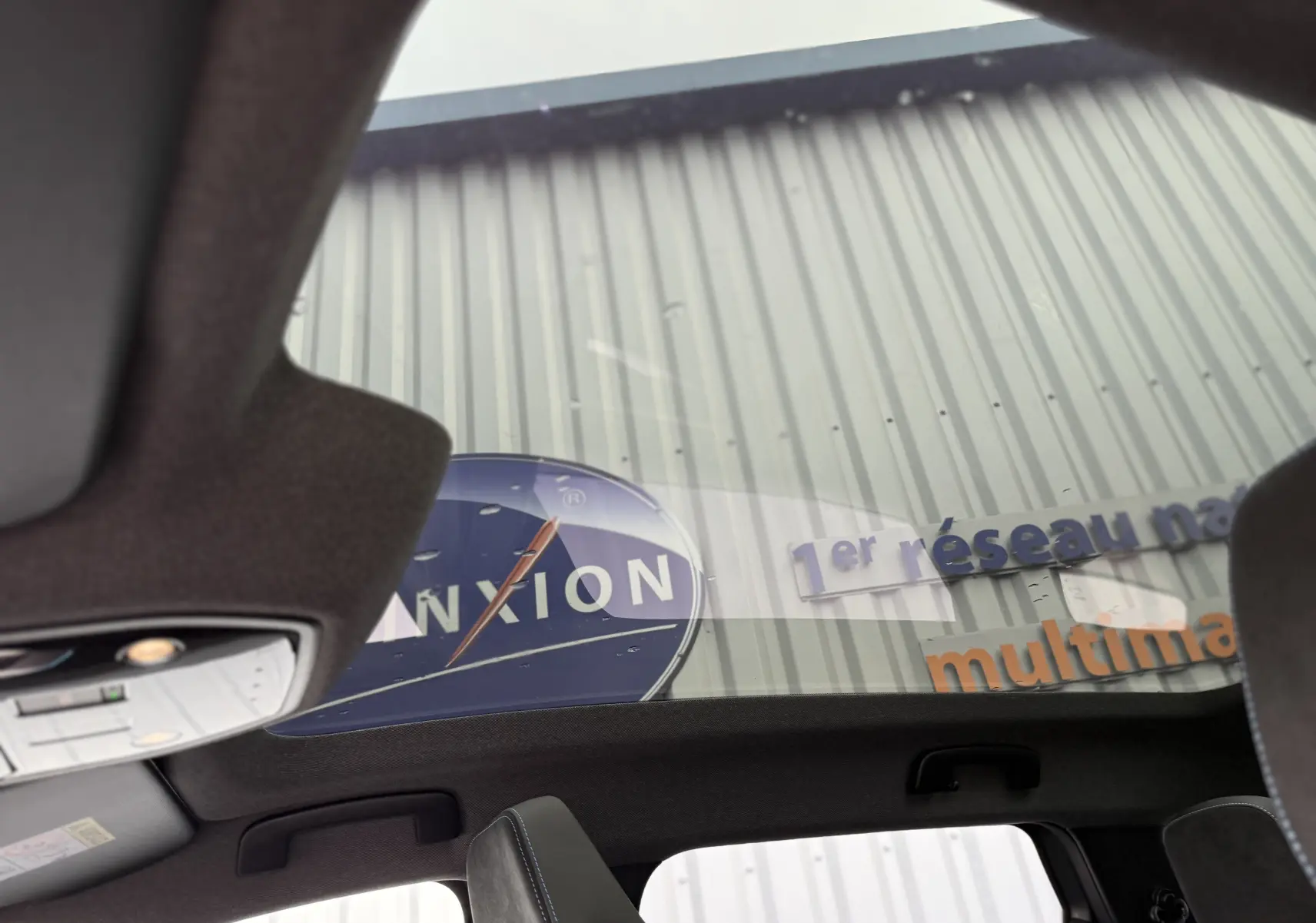 Toit panoramique en verre vu de l'intérieur d'un Renault Espace gris schiste 2025, sièges noirs avec surpiqûres bleues visibles.