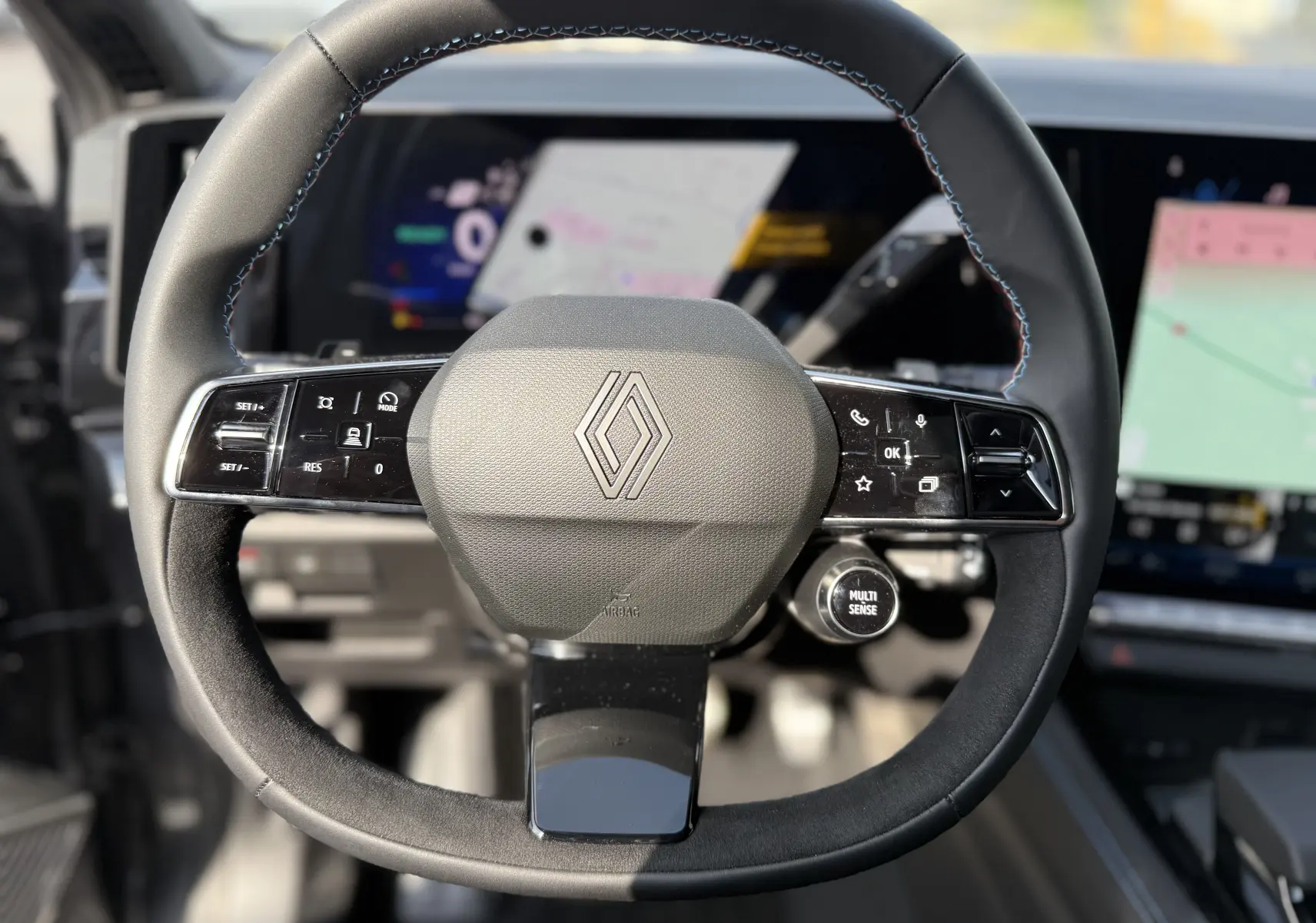 Vue rapprochée du volant noir avec surpiqûres bleues du Renault Espace 2025, affichage numérique en arrière-plan.