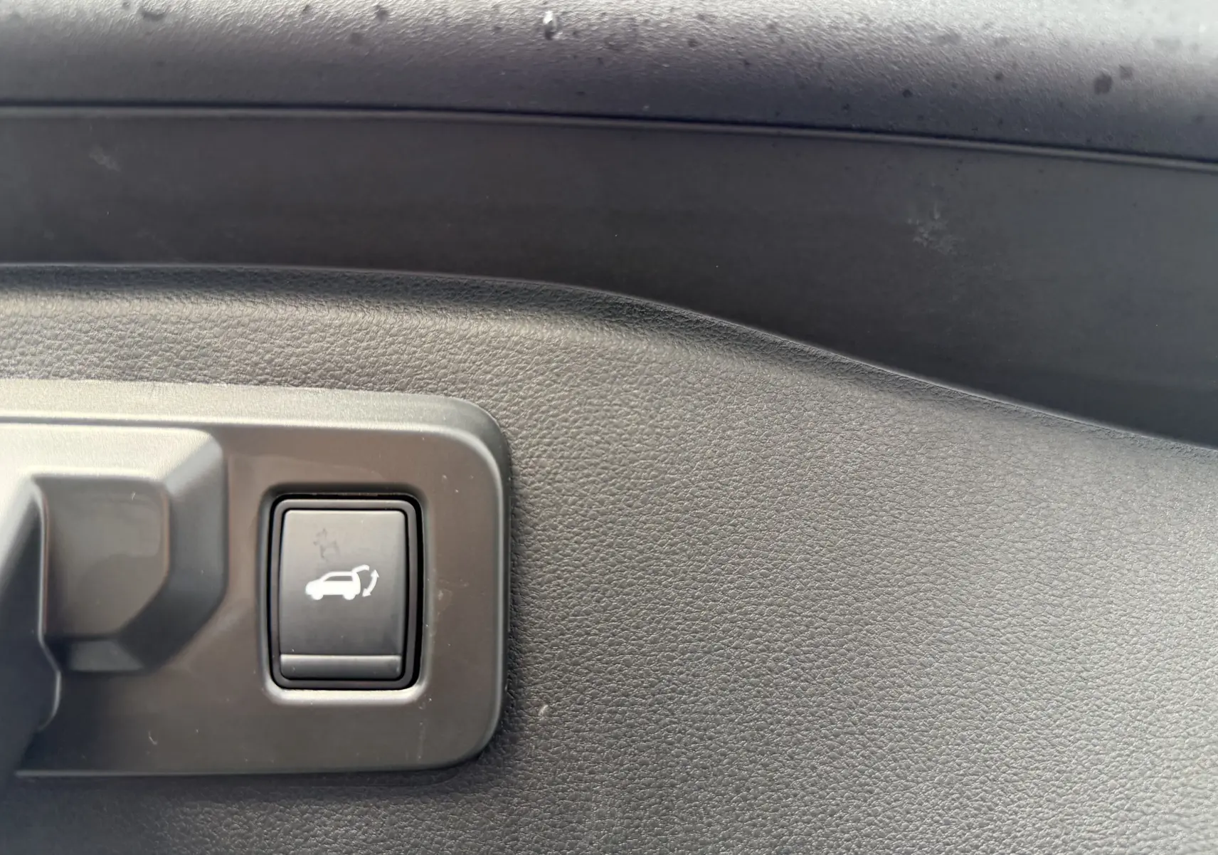 Bouton d'ouverture électrique du hayon sur panneau intérieur noir du Renault Espace gris schiste 2025 hybride.