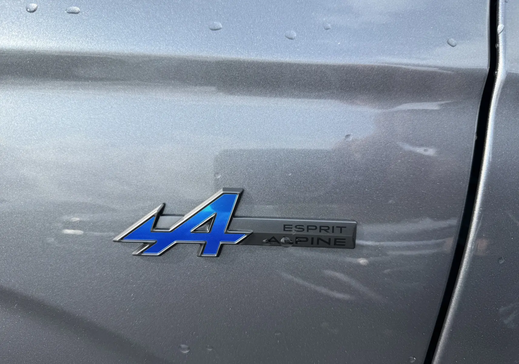 Gros plan sur l'emblème bleu "A" et la mention "Esprit Alpine" sur la carrosserie gris schiste métallisé du Renault Espace.