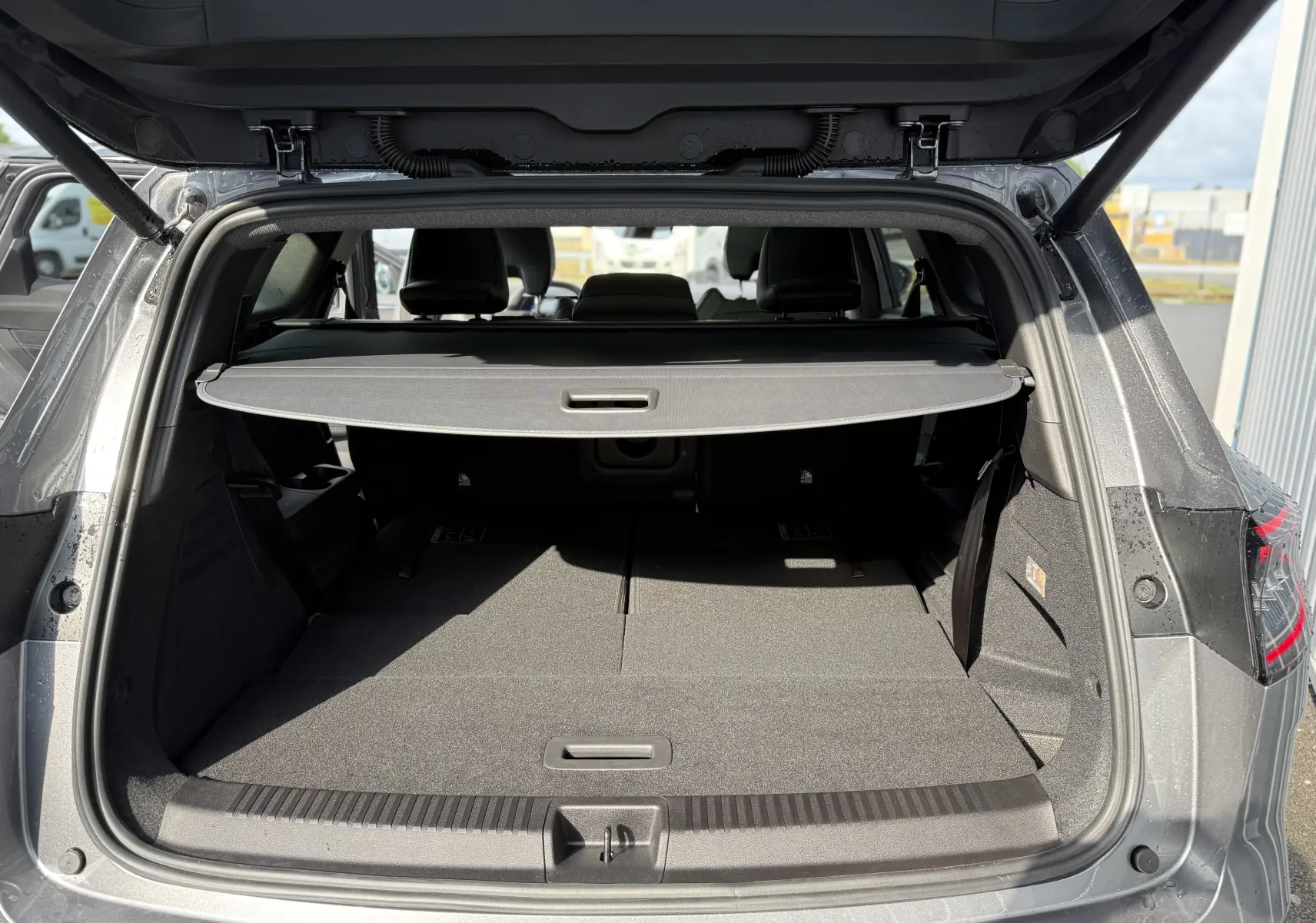 Coffre ouvert vu de l'arrière d'un Renault Espace gris schiste métal avec cache-bagages et sièges rabattus.