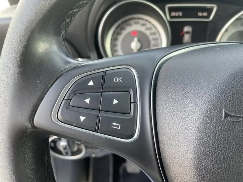 Gros plan sur les commandes gauche du volant noir d’un Mercedes GLA 200 D Sensation 2017 avec tableau de bord en arrière-plan.