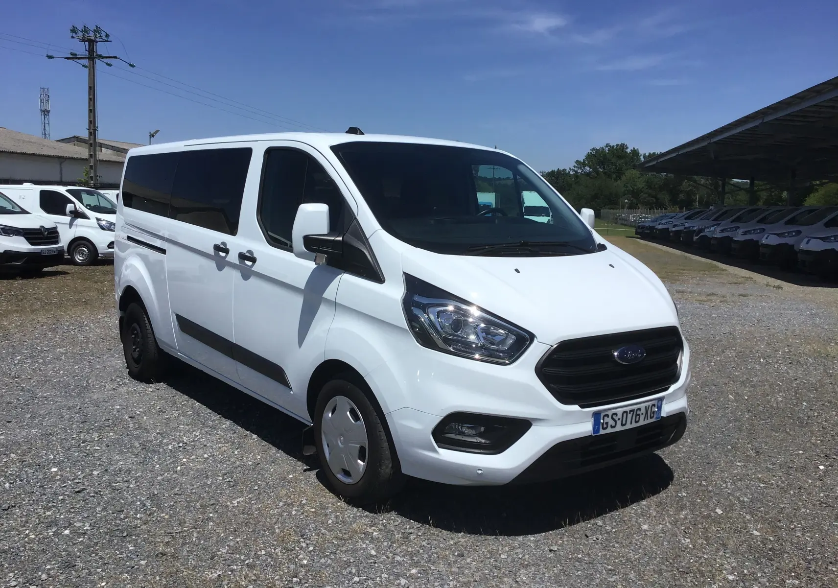 Ford Transit Custom Kombi blanc vu en 3/4 avant droit, avec vitres arrière teintées et jantes acier.
