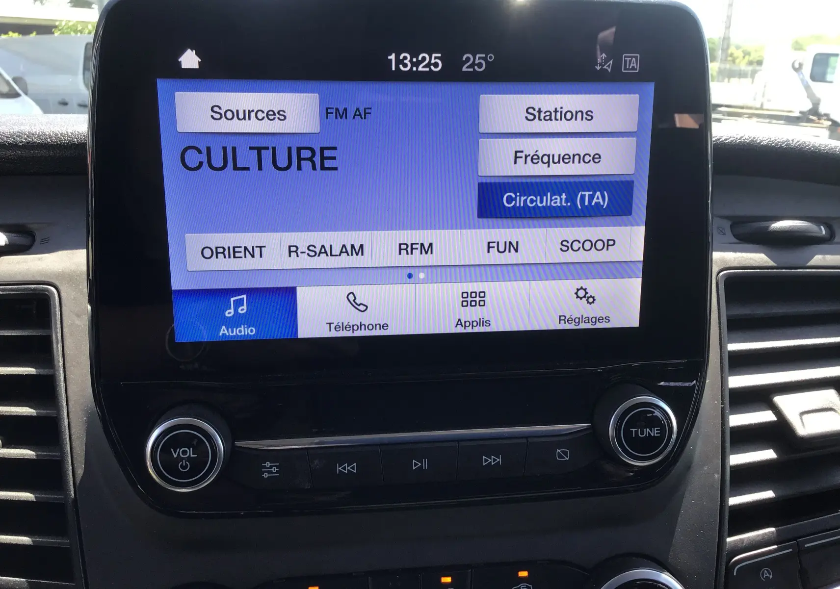 Écran tactile central du Ford Transit Custom Kombi 2023 affichant les options audio et radio, entouré de commandes noires.