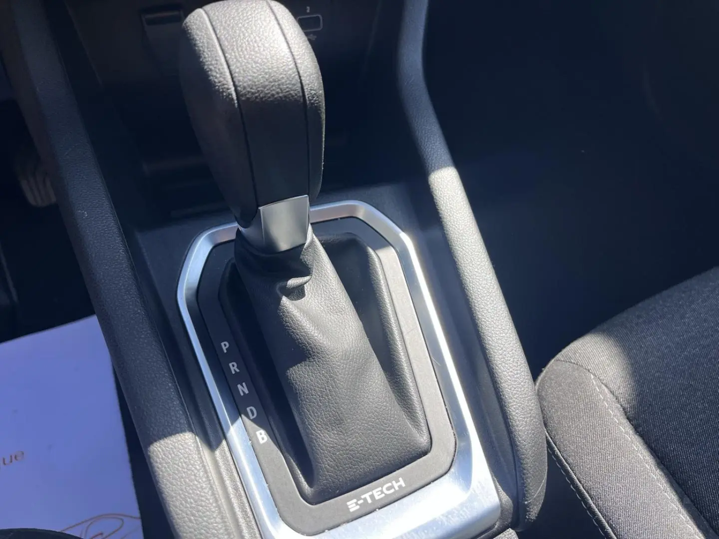 Gros plan sur le levier de vitesses automatique noir avec marquage E-TECH dans l’habitacle d’une Renault Clio blanche.