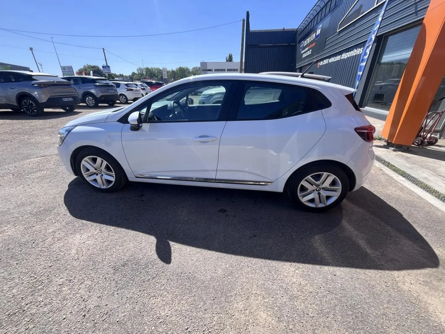 Renault Clio blanc Quartz vue de profil côté gauche sur parking ensoleillé avec jantes alliage.