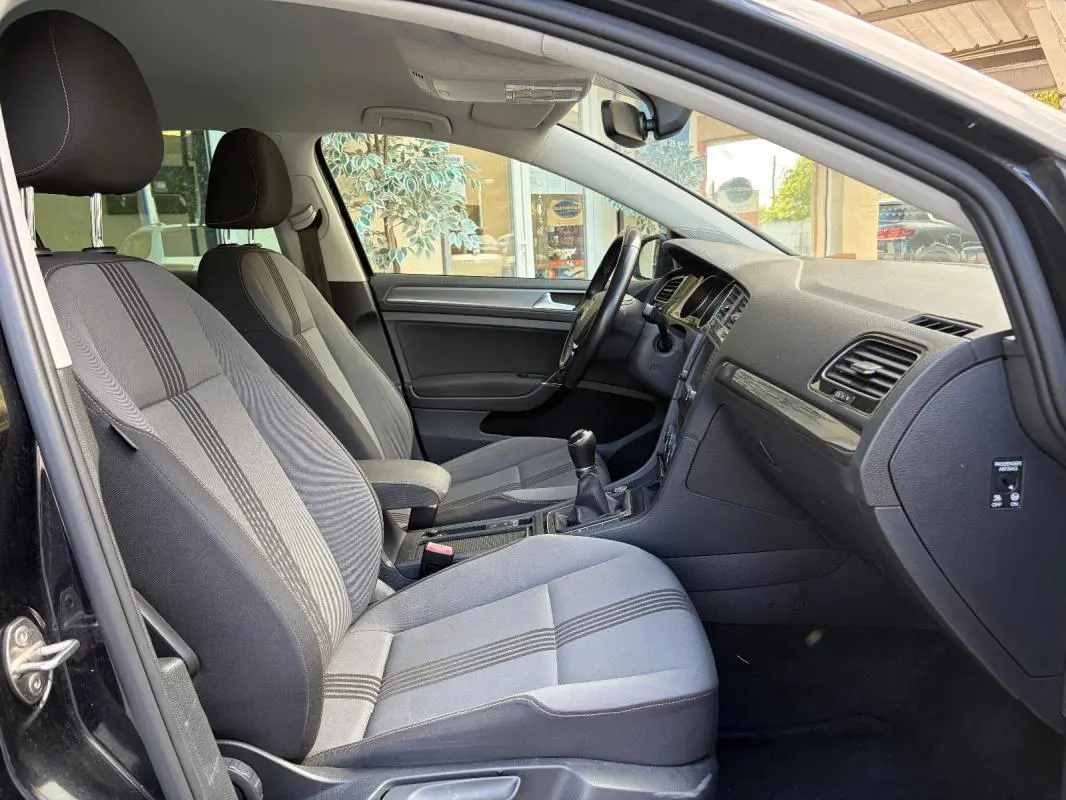 Intérieur côté conducteur de la Volkswagen Golf 7 noire, montrant sièges tissu, volant cuir multifonctions et boîte manuelle.