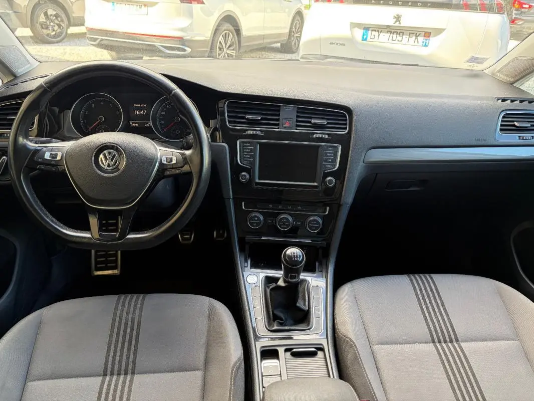 Vue intérieure avant de la Volkswagen Golf 7 noire, volant cuir multifonctions et levier de vitesse manuel visibles.