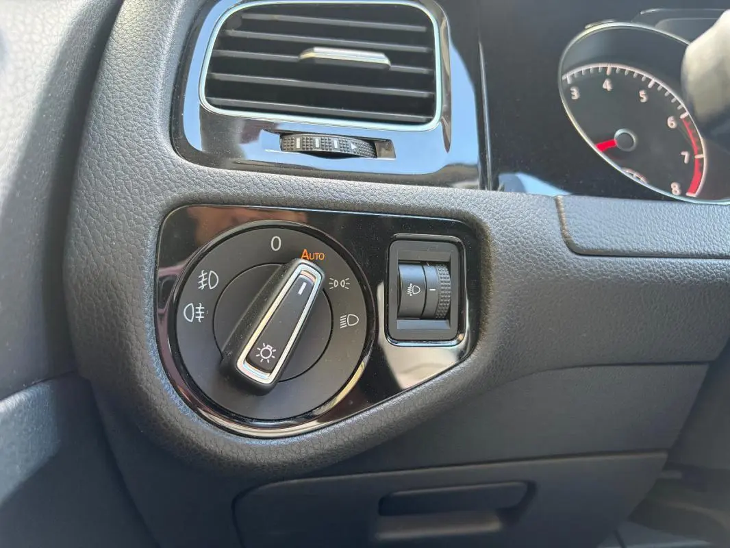 Gros plan sur le bouton de commande des phares et la molette de réglage de l’éclairage dans l’habitacle d’une Volkswagen Golf noire.