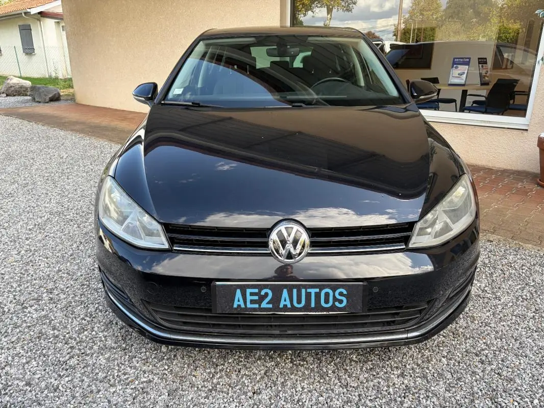 Vue frontale d'une Volkswagen Golf 7 noire, avec calandre et logo VW bien visibles sur un sol gravillonné.