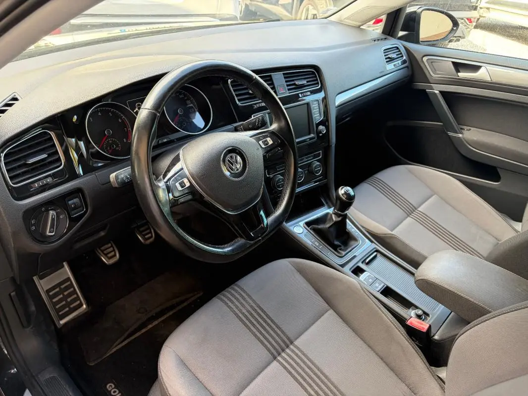 Vue intérieure côté conducteur de la Volkswagen Golf 7 noire, volant cuir multifonctions et levier de vitesse manuel visibles.