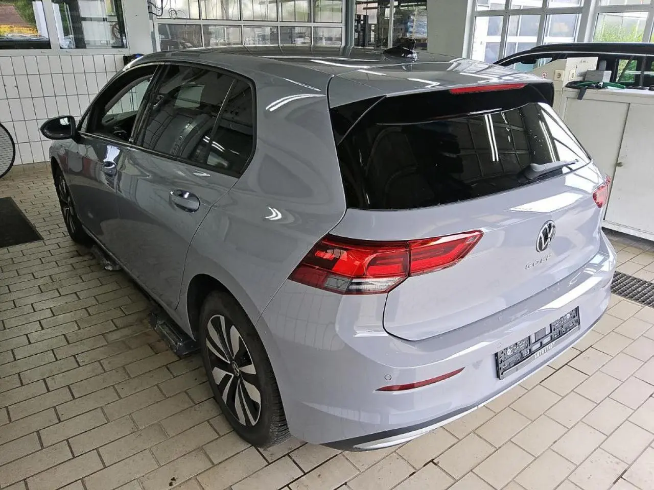 Volkswagen Golf 8 gris lunaire vue 3/4 arrière droit, feux arrière LED et vitres teintées dans un garage.