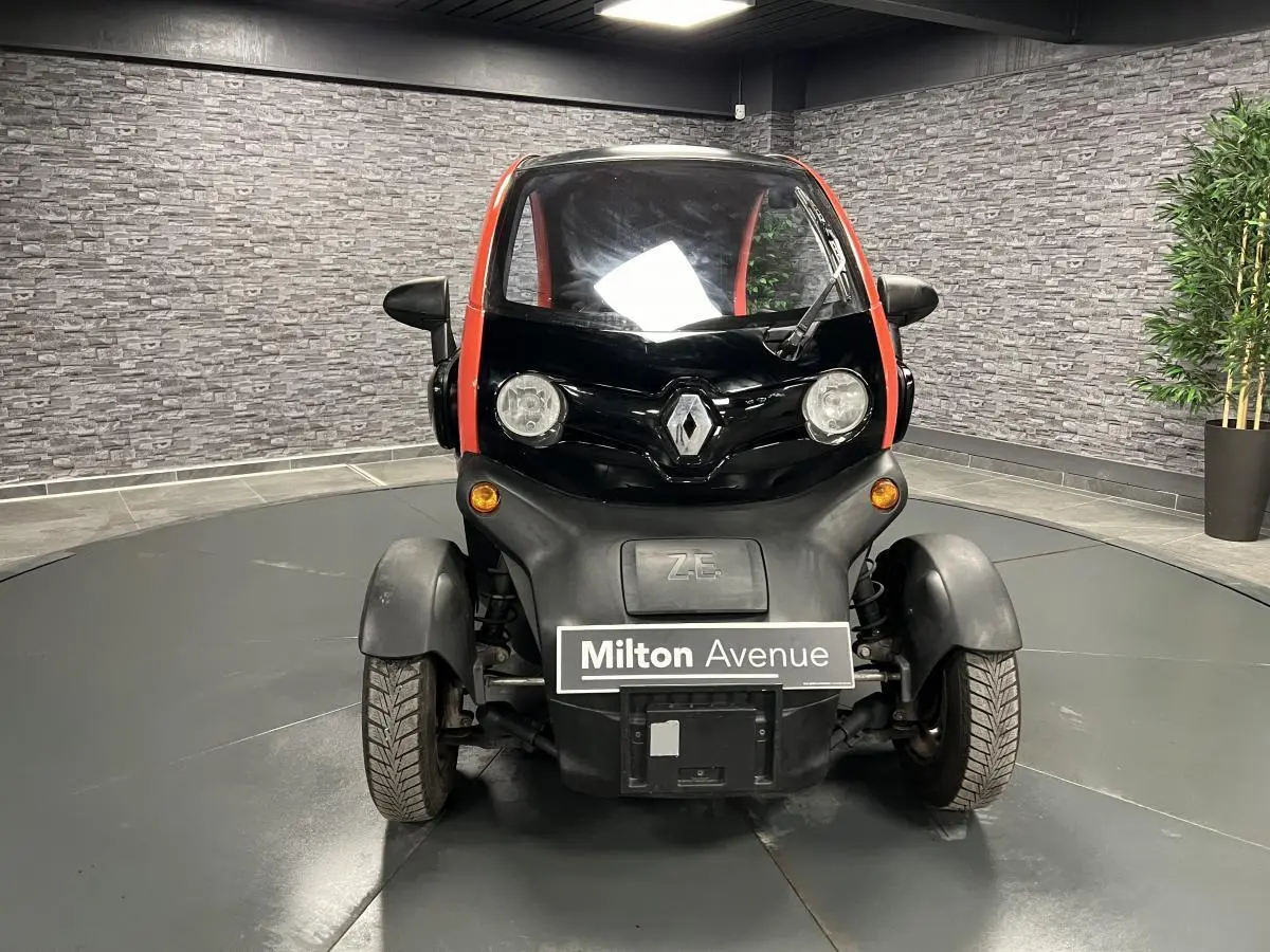 Vue frontale d'une Renault Twizy Intens 2019 orange avec logo Renault et phares ronds dans un showroom.