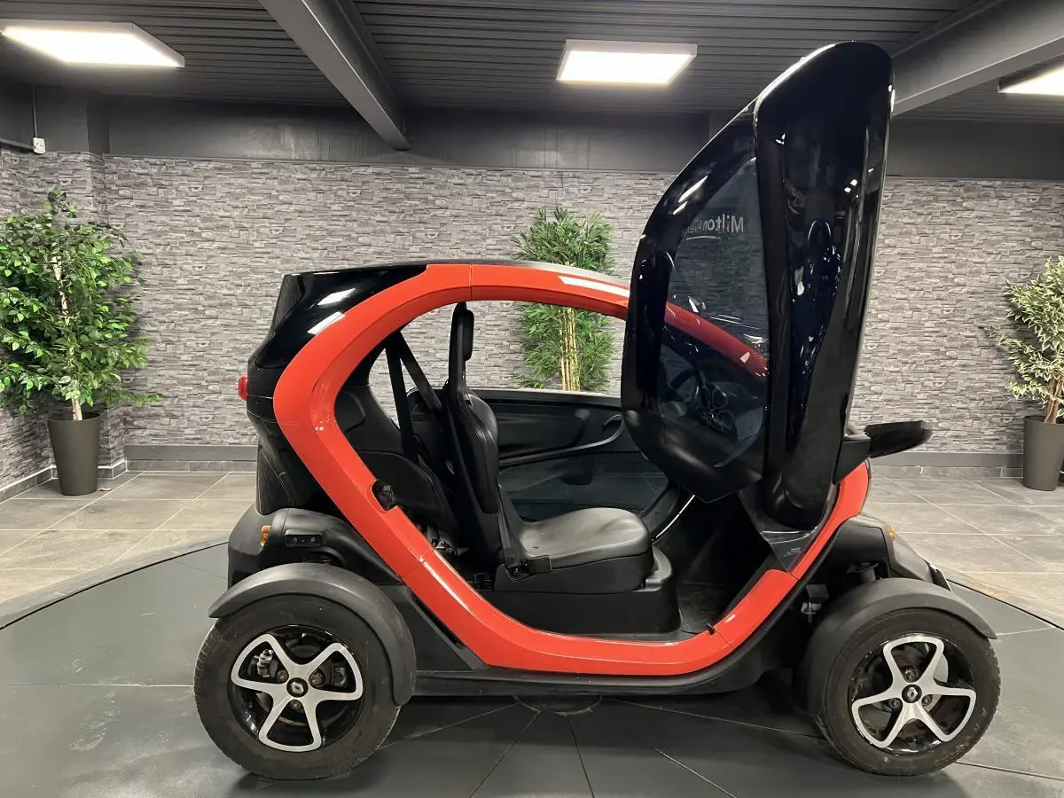 Profil droit d'une Renault Twizy orange 2019 avec porte élytre ouverte, montrant l'intérieur compact et les sièges noirs.