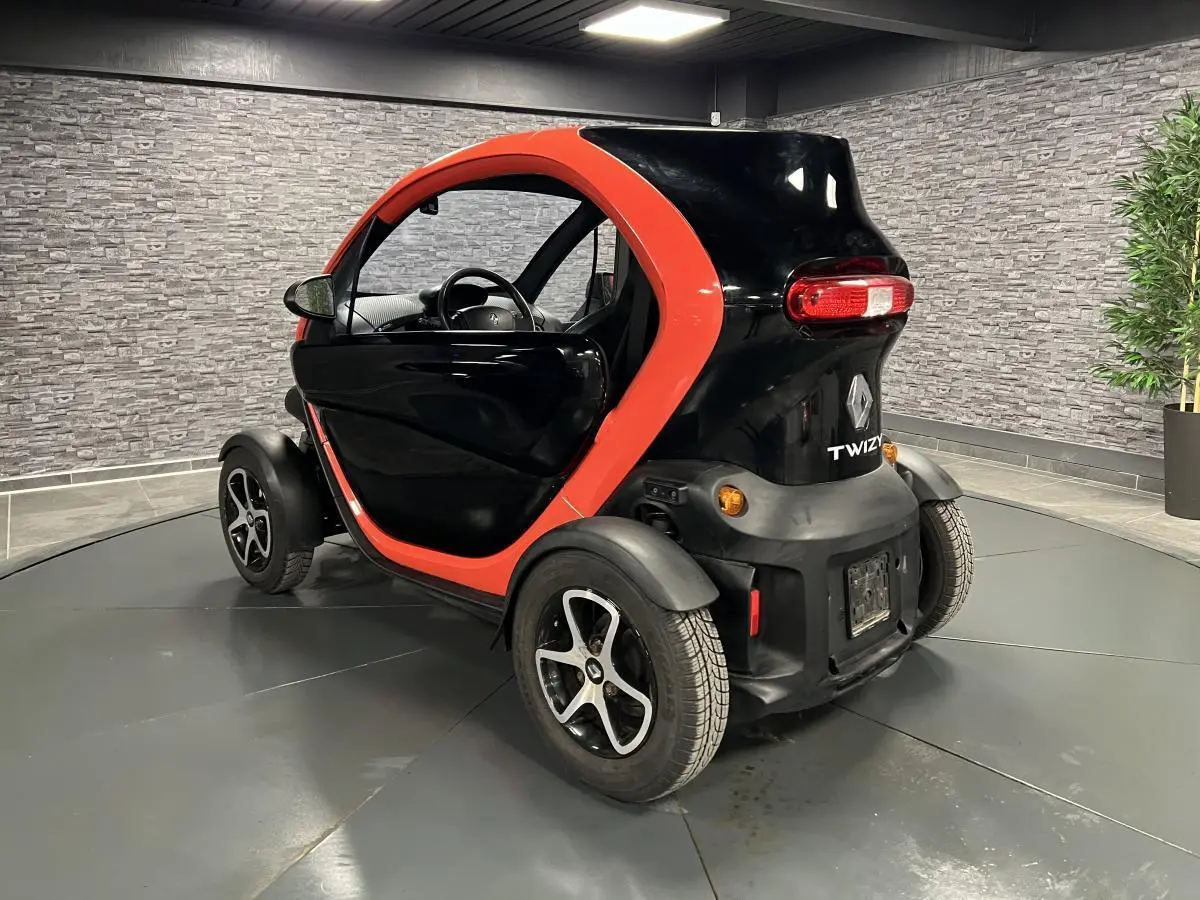 Vue 3/4 arrière droite d'une Renault Twizy Intens 2019 orange et noire avec portes élytre dans un showroom.