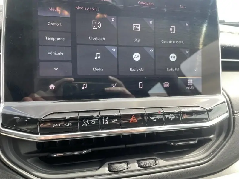 Écran tactile central du Jeep Compass 2024 blanc montrant les options média et les commandes de sécurité en dessous.