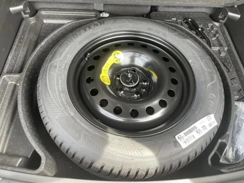 Roue de secours noire avec étiquette jaune dans le coffre d'un Jeep Compass blanc 2024 hybride essence.