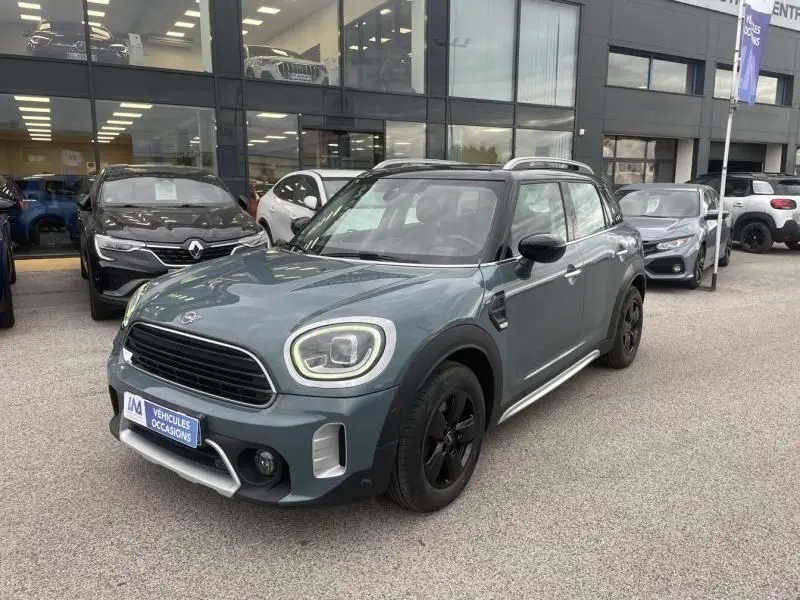Vue 3/4 avant d'une MINI Countryman Cooper 136 gris avec toit noir et jantes noires, stationnée devant un showroom.
