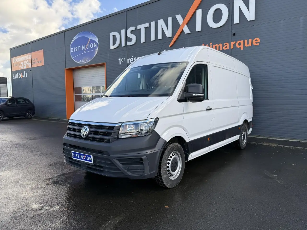 Volkswagen Crafter fourgon blanc vu en 3/4 avant droit devant un bâtiment gris avec logo Distinxion.