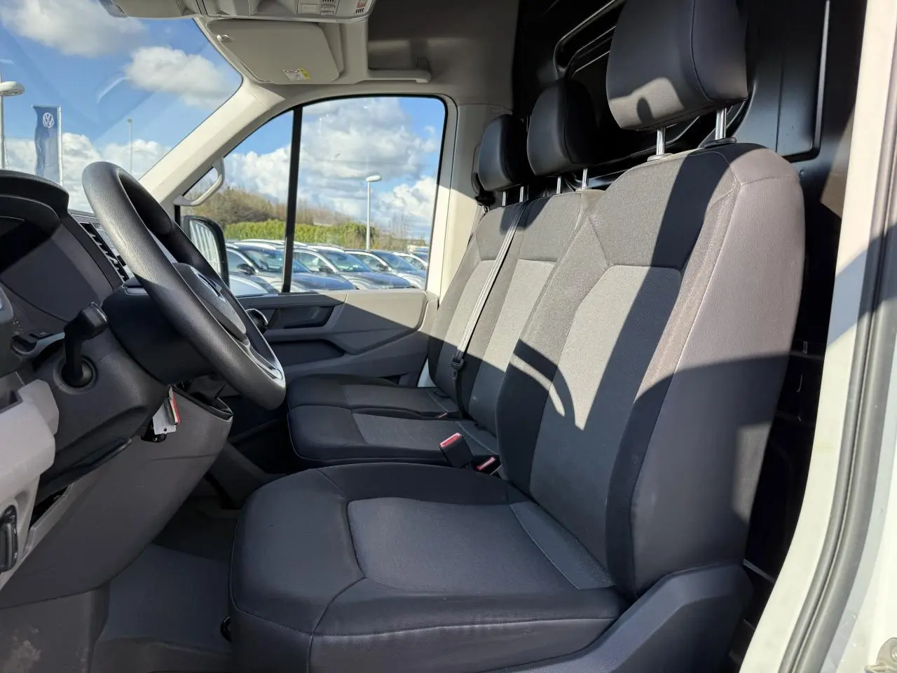 Vue intérieure côté conducteur du Volkswagen Crafter blanc, montrant les sièges avant en tissu gris et le volant multifonctions.
