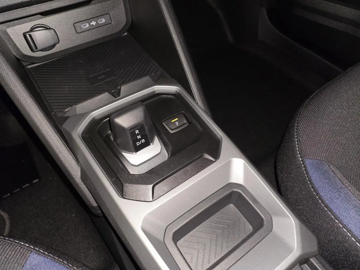 Vue rapprochée de la console centrale grise et noire du Dacia Duster 1.6 Hybrid 2025 avec levier de vitesses automatique et siège tissu Denim bleu.