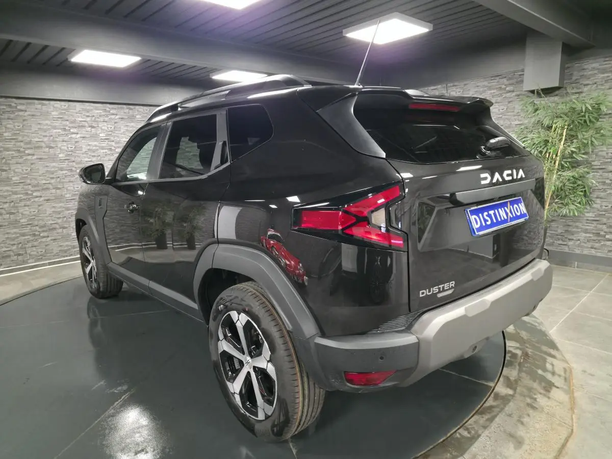 Vue 3/4 arrière droit du Dacia Duster 1.6 Hybrid noir nacré avec jantes alliage 18 pouces et barres de toit noires.