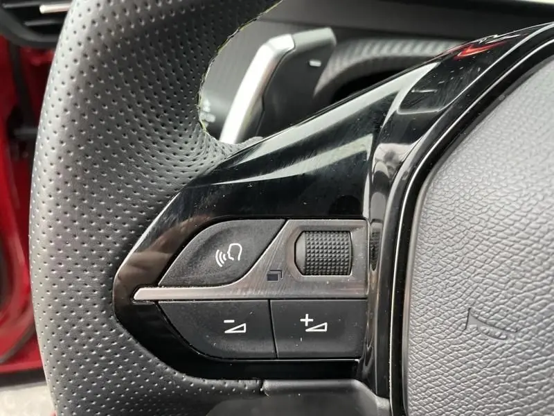 Gros plan sur les commandes au volant côté gauche du Peugeot 2008 130 GT-LINE rouge métal, avec boutons de volume et micro intégrés.