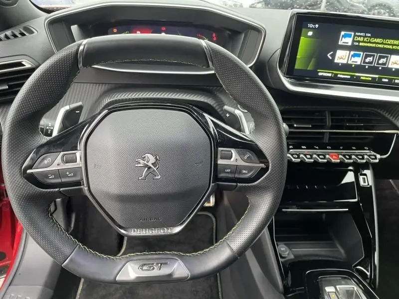 Vue rapprochée du volant GT et du tableau de bord numérique d’une Peugeot 2008 130 GT-LINE rouge métal de 2022.