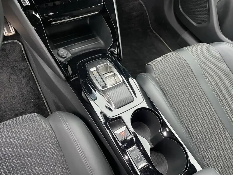 Vue rapprochée de la console centrale noire brillante du Peugeot 2008 130 GT-LINE rouge métal, avec levier de boîte auto et porte-gobelets.
