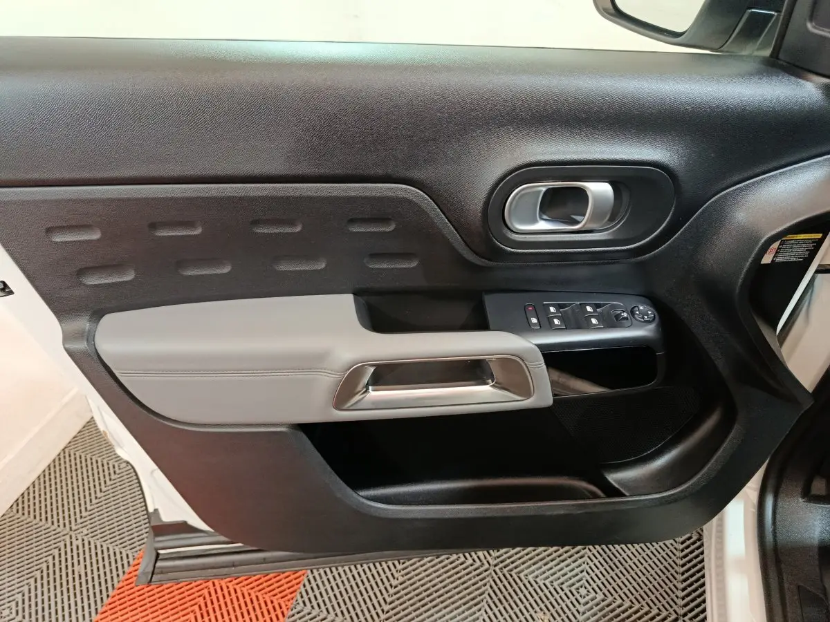 Vue rapprochée de la porte avant gauche noire et grise du Citroën C5 Aircross Hybrid 225 ë-EAT8 avec commandes de vitres et poignée métallique.