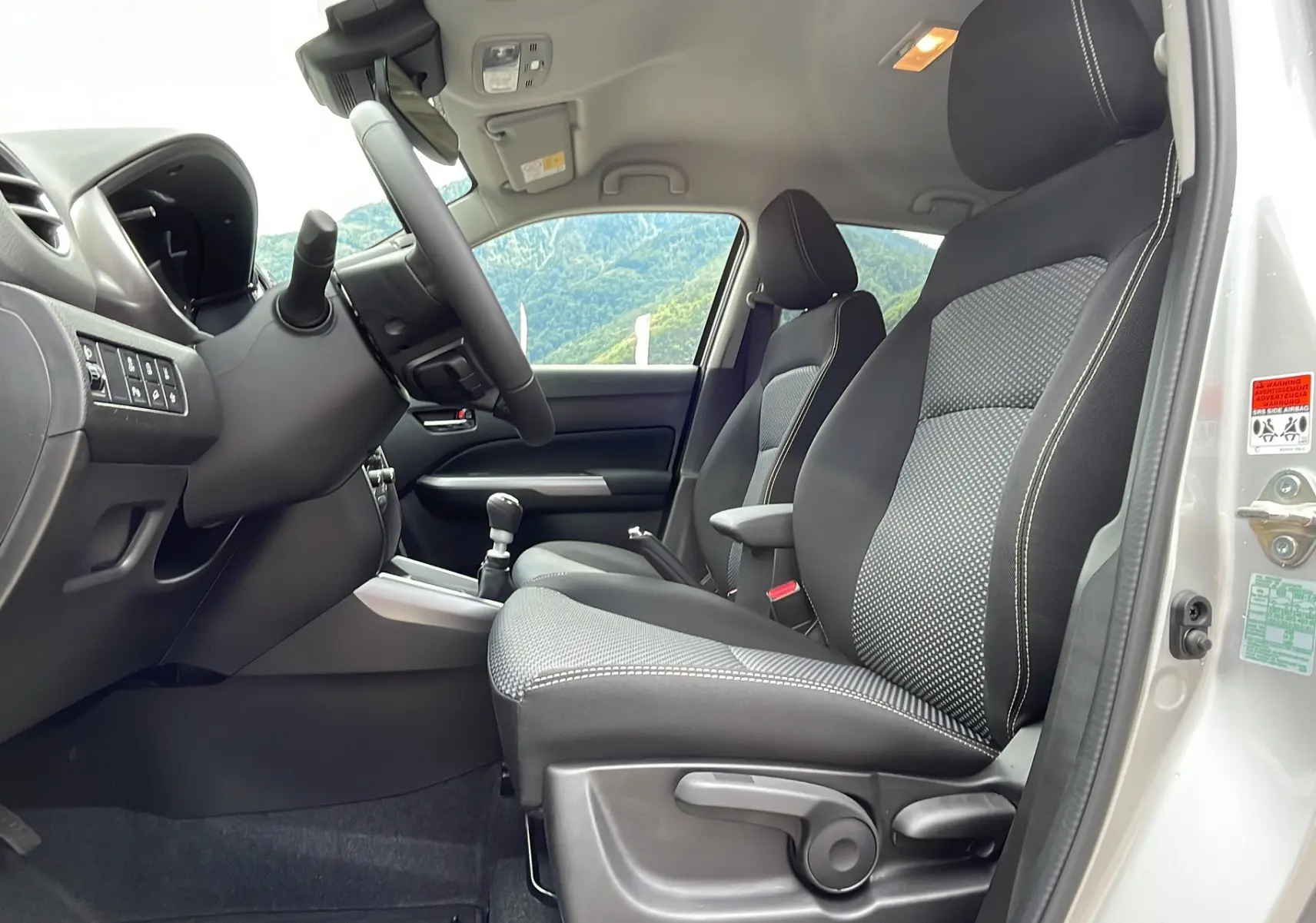 Vue intérieure côté conducteur du Suzuki Vitara 2025 gris argent avec sièges tissu noir et volant multifonctions.