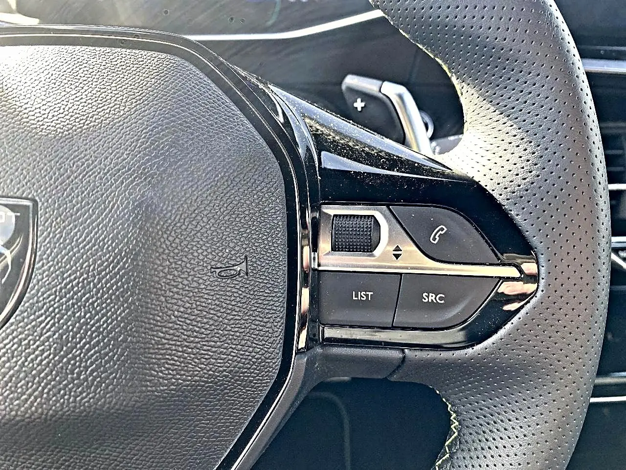 Gros plan sur le volant cuir perforé du Peugeot 2008 1.2 hybrid 145 GT, avec commandes multifonctions et palettes au volant.