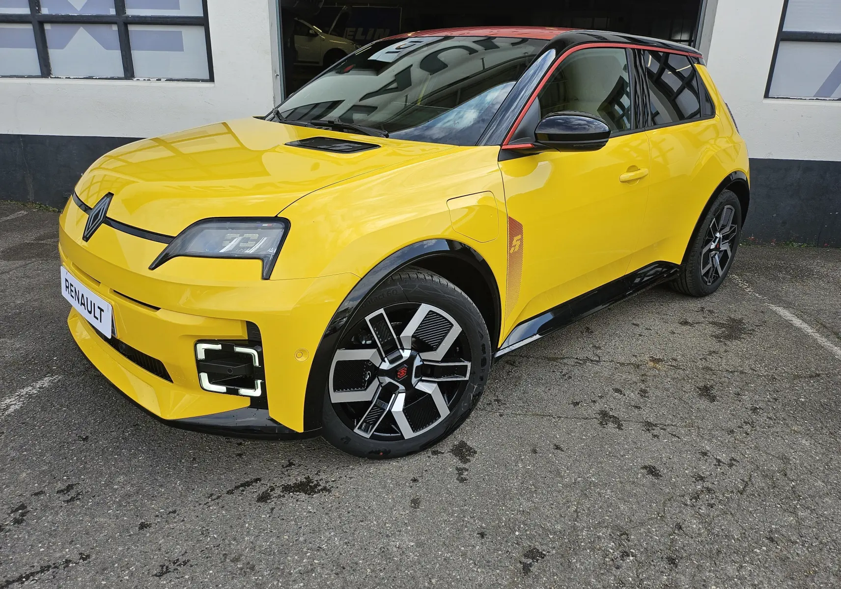 Renault R5 Iconic 2025 vue 3/4 avant en jaune pop avec toit noir et jantes au design futuriste.