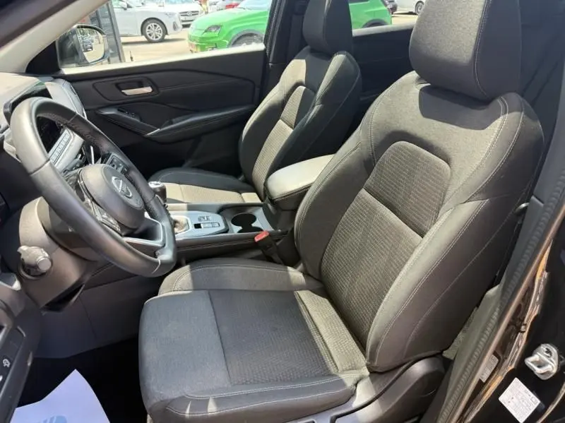 Vue intérieure côté conducteur du Nissan Qashqai 2023 noir, mettant en valeur les sièges en tissu et la console centrale avec boîte manuelle.