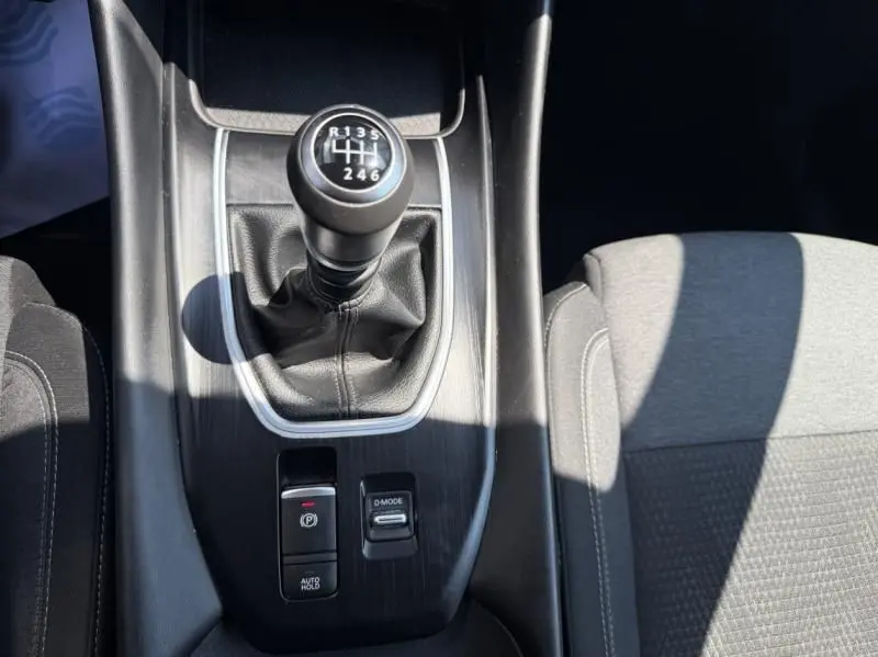 Le levier de vitesses manuel noir du Nissan Qashqai 1.3 Mild Hybrid 2023 vu de dessus avec console et siège gris.