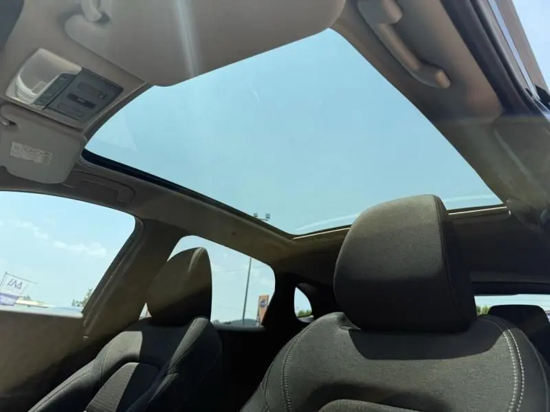 Intérieur du Nissan Qashqai 2023 noir, vue sur les sièges avant et le grand toit panoramique sous un ciel bleu.