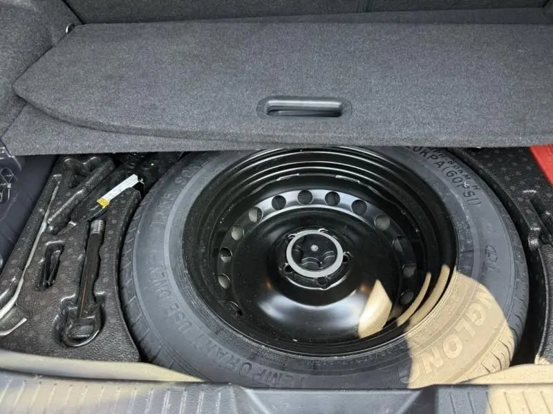 Roue de secours noire et outils de bord visibles dans le coffre du Nissan Qashqai 1.3 Mild Hybrid 2023.