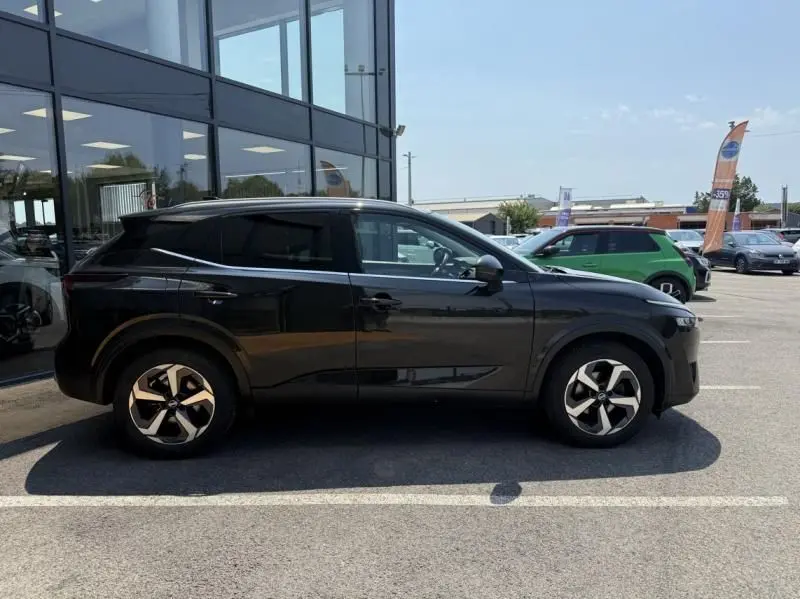 Profil côté gauche du Nissan Qashqai noir 2023, version 1.3 Mild Hybrid N-Connecta, stationné devant un bâtiment vitré.