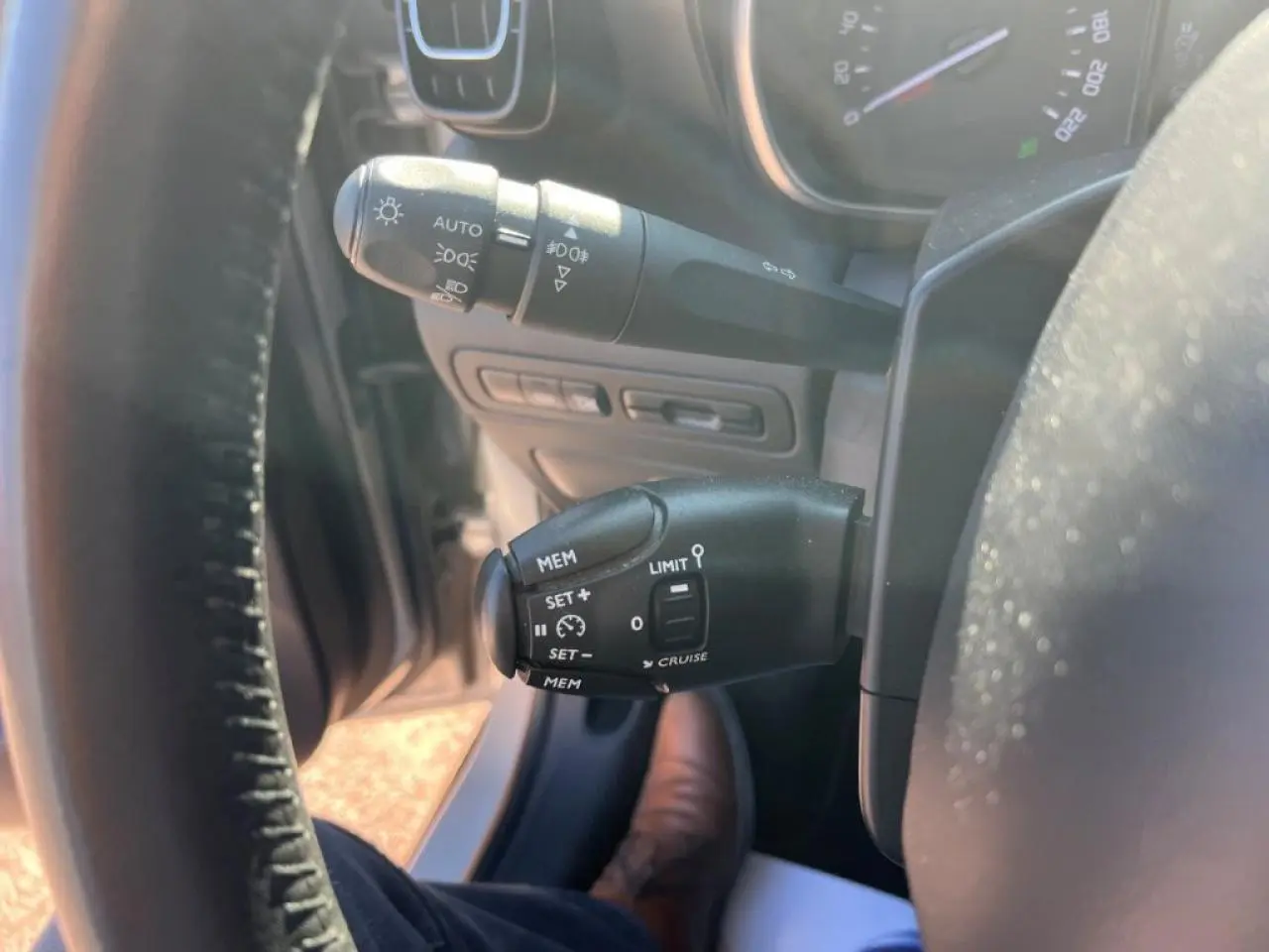 Gros plan sur les commandes de régulateur de vitesse et éclairage à gauche du volant d'une Citroën C3 Aircross beige.