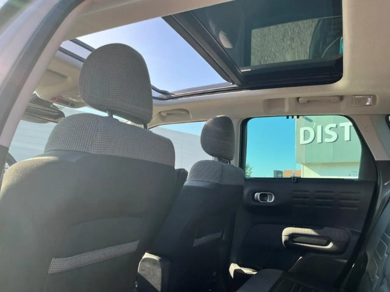 Vue intérieure arrière du Citroën C3 Aircross beige, mettant en valeur le toit ouvrant panoramique et les sièges en tissu et cuir noir.