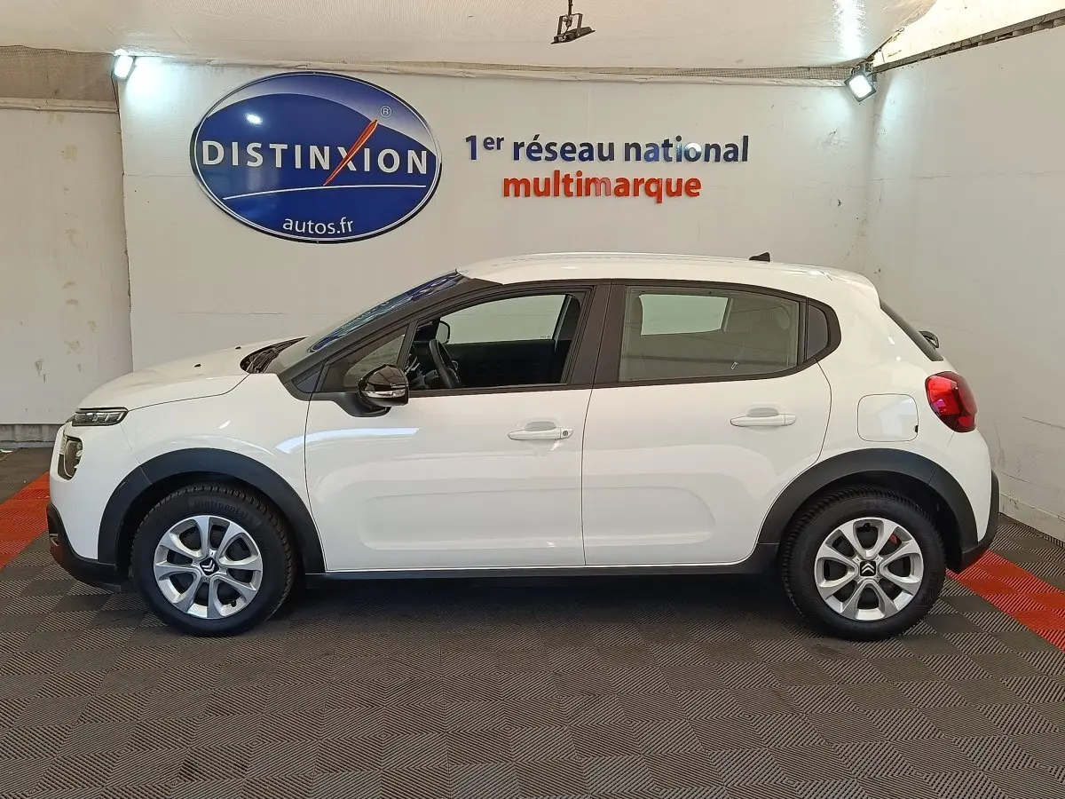 Profil côté gauche d'une Citroën C3 blanche 2020 avec jantes alliage et rétroviseurs noirs dans un showroom.