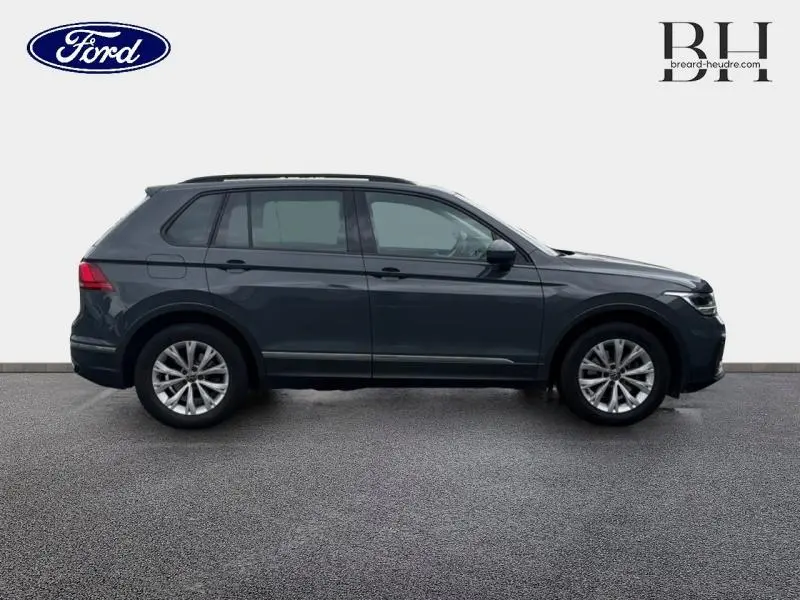 Vue de profil côté gauche d'un Volkswagen Tiguan gris dauphin métallisé avec barres de toit et jantes alu.