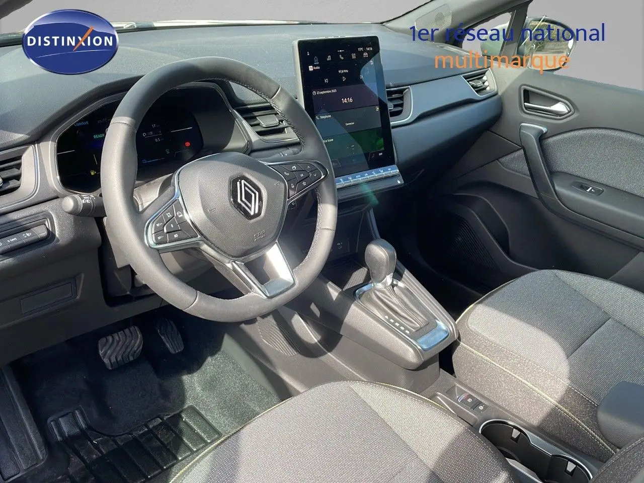 Vue intérieure de la Renault Captur 2025 montrant le volant, la console centrale avec écran tactile et les sièges tissu gris.
