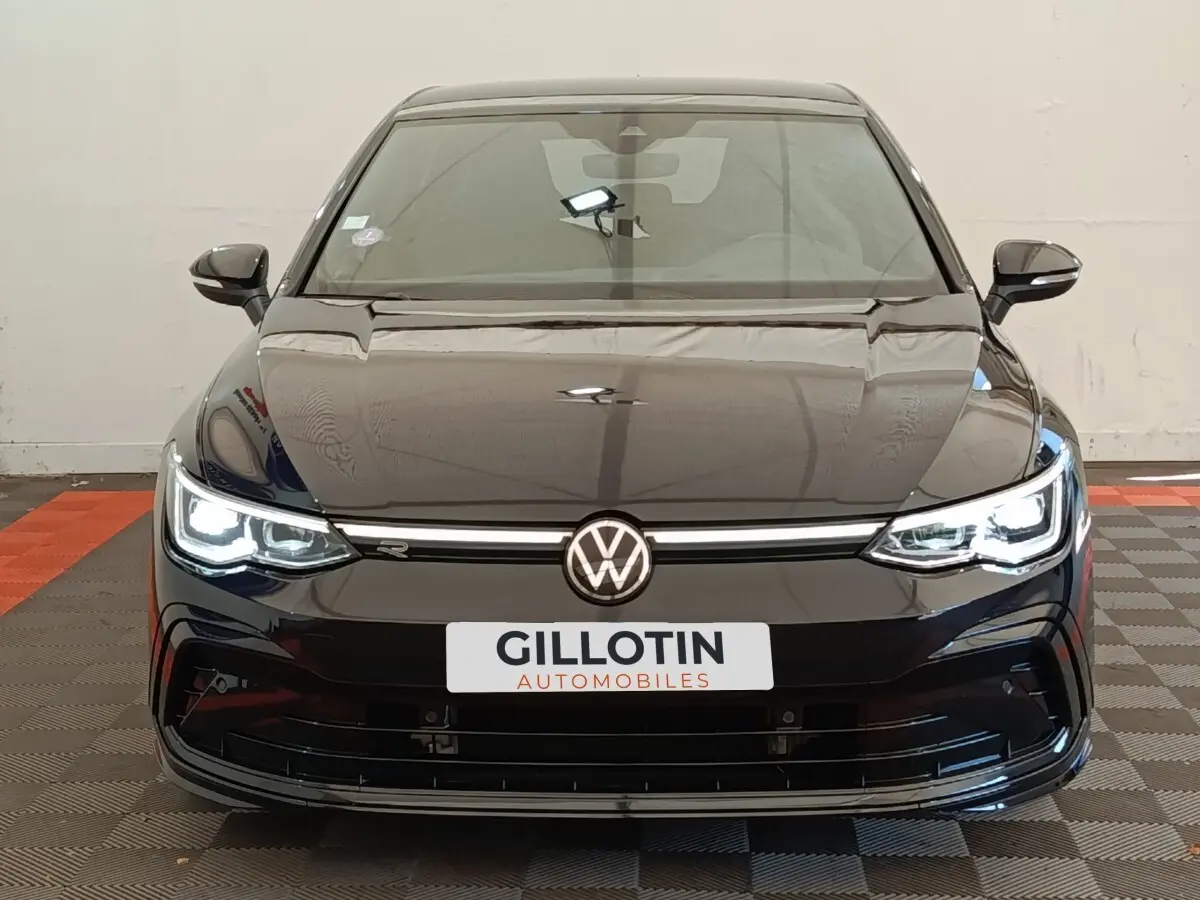 Vue frontale d'une Volkswagen Golf 1.5 eTSI noire avec phares LED allumés et logo R-Line visible sur la calandre.