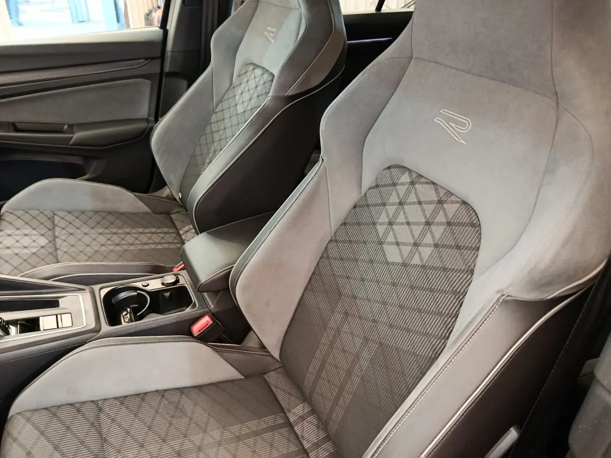 Vue rapprochée des sièges avant gris et noirs de la Volkswagen Golf 1.5 eTSI R-Line avec surpiqûres et logo R-Line brodé.