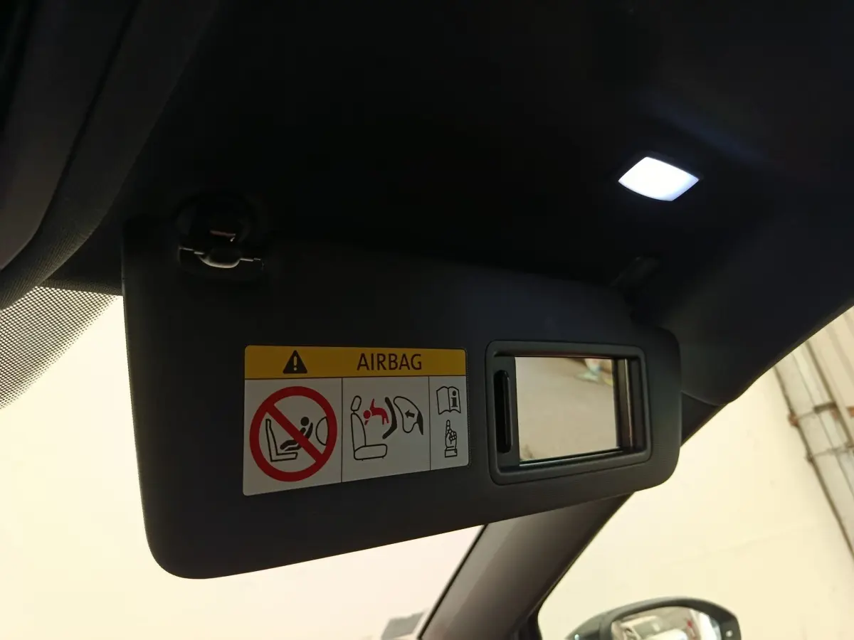 Détail intérieur du pare-soleil côté conducteur avec miroir et avertissement airbag, dans une Volkswagen Golf noire.