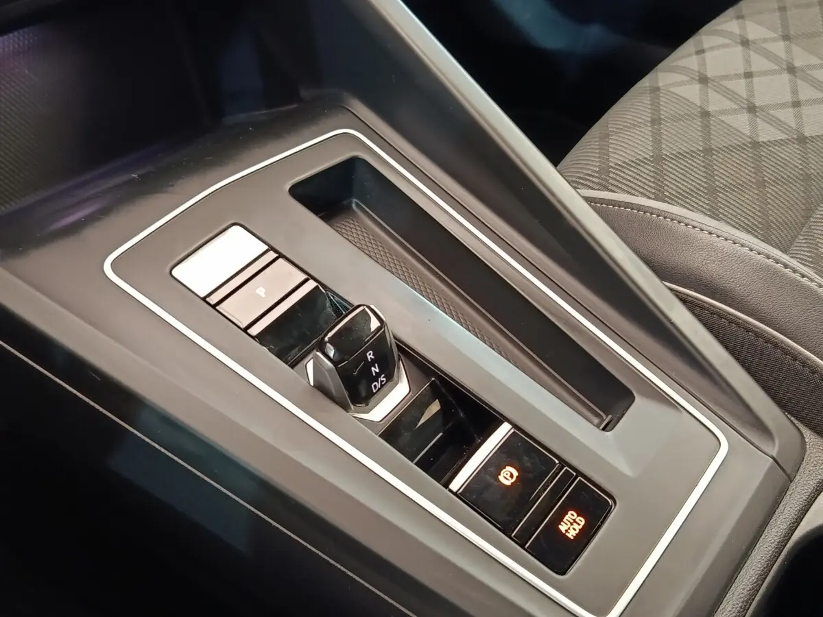 Gros plan sur la console centrale noire de la Volkswagen Golf 1.5 eTSI avec levier de vitesses automatique et boutons de frein à main électronique.